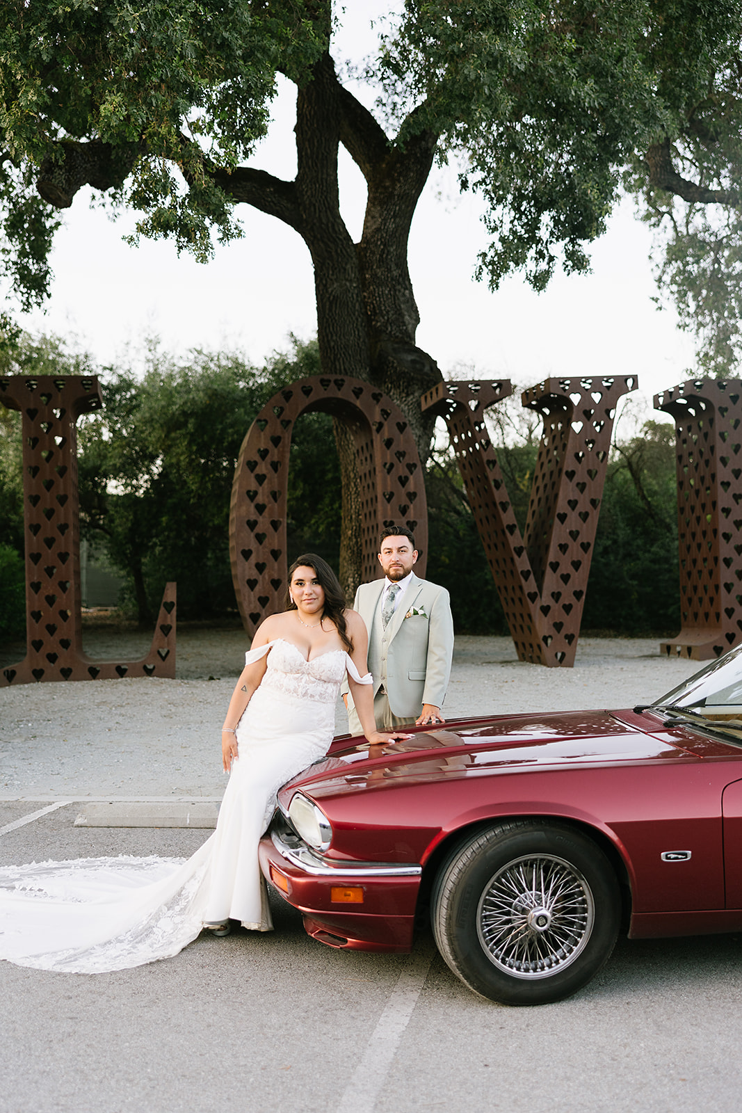 Bride & Groom portrait standing by leaning on the hood of a red vintage jaguar.