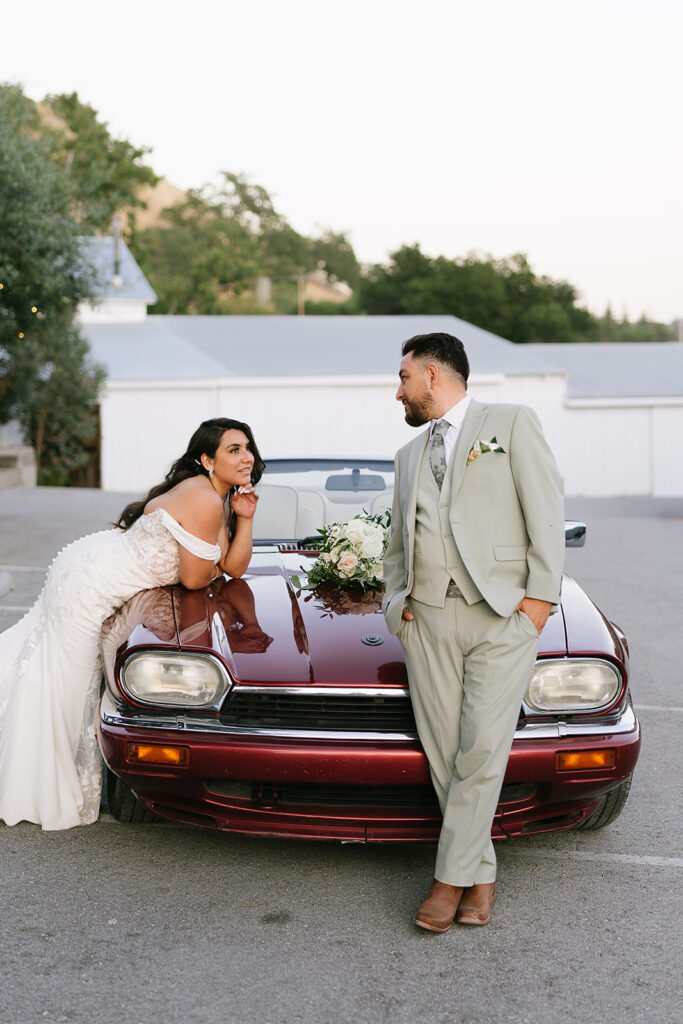 Bride & Groom portrait standing by leaning on the hood of a red vintage jaguar.