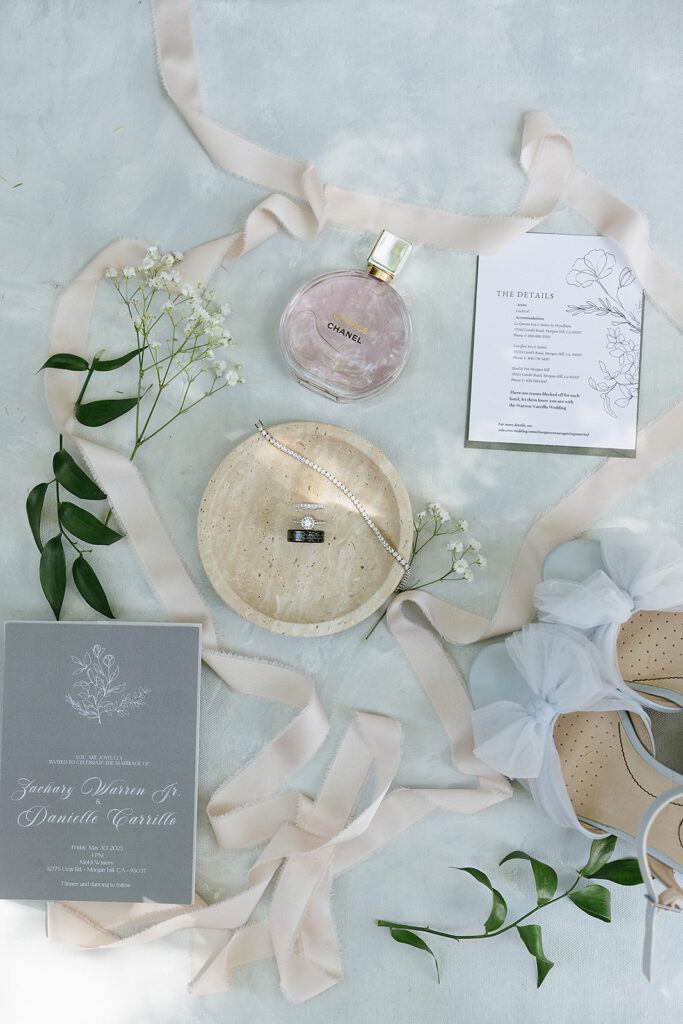 Flat lay of wedding invitation with Chanel perfume blue shoes and a pinkish ribbon 