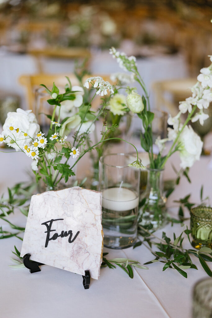 Stone table sign with the word four with flowers in bud vases and candles floating in water vases 