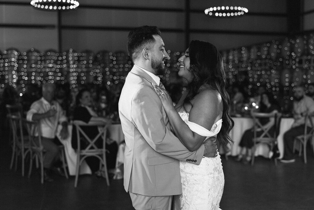 black and white photo of c couple smiling with guest in the background 